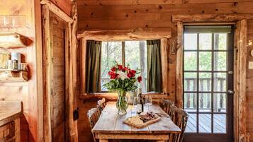 L'intérieur d'un chalet en bois rustique, avec une table à manger, des chaises, un vase rempli de fleurs et une bouteille de vin.
