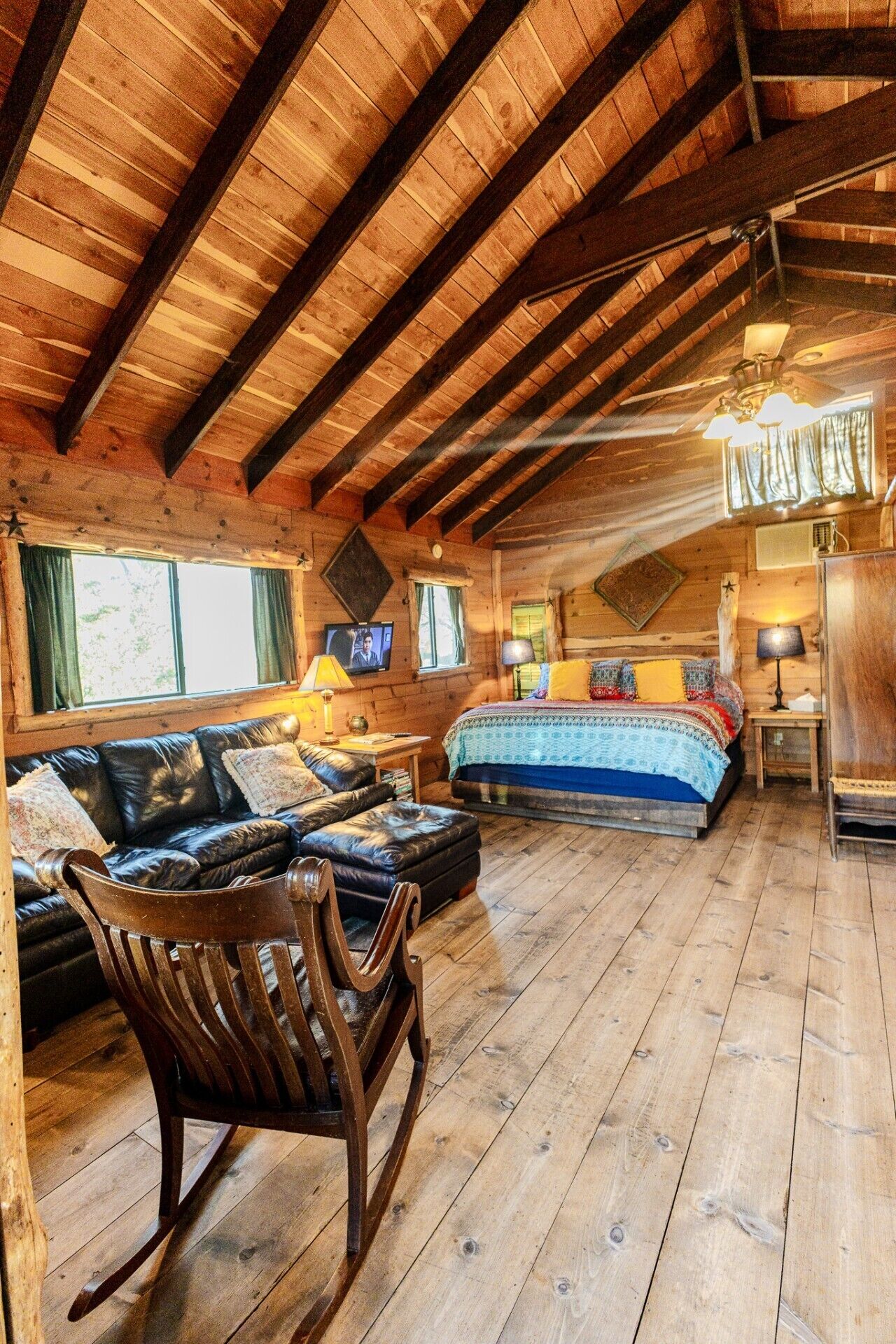 L’intérieur d’une cabane en rondins, avec une chambre à coucher aménagée en mezzanine, un canapé en cuir, un fauteuil à bascule et un plancher en bois.