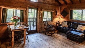 Interior rústico de una cabaña con una mesa de comedor de madera, sillas, un sofá de cuero y un ventilador de techo.