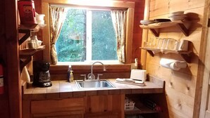 Eine Holzhütte mit Küche, ausgestattet mit Fenster, Spüle, Kaffeemaschine und Regalen mit Geschirr.