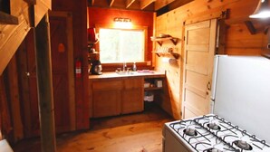Eine kompakte Küche mit Gaskochfeld, Holzschränken, einem Spülbecken und einem Fenster.