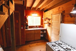 Pieni, käytännöllinen keittiö, jossa on kaasuliesi, puukaapit, pesuallas ja ikkuna.