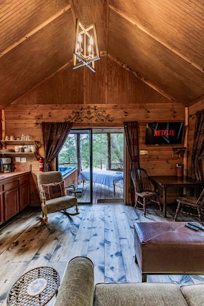 L’intérieur chaleureux d’un chalet avec un plafond en bois, un coin repas, un téléviseur et une vue par la fenêtre.