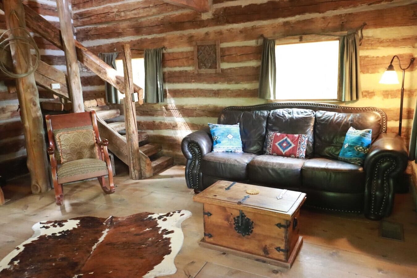 A log cabin interior with a leather sofa, a wooden chair, a cowhide rug, and a chest of drawers.