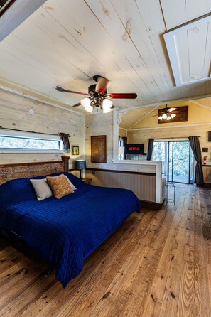 Ein Schlafzimmer mit einem großen Bett, einem Deckenventilator, Holzboden und Blick ins Freie.