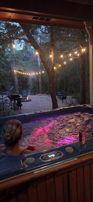 Ein Whirlpool mit Blick auf bewaldetes Gelände, Lichterketten und Sitzmöglichkeiten im Freien.