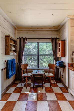 Ein Zimmer mit Schachbrettmuster-Boden, einem Vorhangfenster, einem Tisch mit Stühlen und Holzschränken.