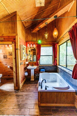 Interno di una baita in legno con bagno, dotato di vasca, lavandino e finestra con tende.