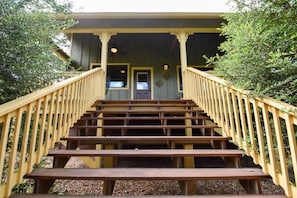 A wooden staircase leading to a porch with a railing, surrounded by trees.