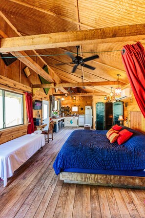 Interno di una baita in legno con un letto, una scrivania, un angolo cottura e una ventola a soffitto.