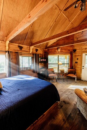 A wooden cabin interior with a large bed, a fireplace, a television, and a balcony.