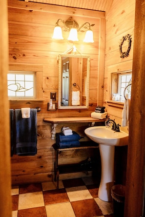 Un baño de cabaña de madera con un espejo, tres lámparas, un lavamanos y un suelo a cuadros.