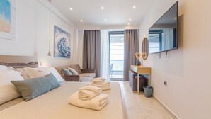 Habitación de hotel con cama, sofá, escritorio, televisor y vista al mar.