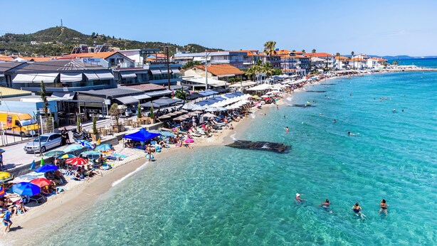 Un pueblo costero con playa, aguas azules cristalinas y edificios a lo largo de la orilla.
