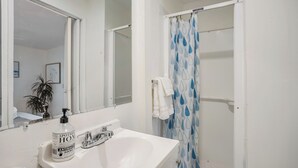 A bathroom with a white sink, a mirror, a shower curtain with a blue leaf pattern, and a bottle of hand sanitizer. - Beach Bungalow Parking 2blocks to Beach (San Diego)