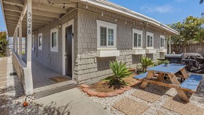A single-story house with a covered porch, a barbecue grill, and a small garden area with plants and a wooden table. - Beach Bungalow Parking 2blocks to Beach (San Diego)