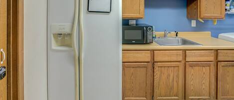A kitchen with a white refrigerator, wooden cabinets, a microwave, and a sink.
