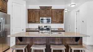 Une cuisine avec des meubles en bois foncé, des appareils électroménagers en acier inoxydable et un grand îlot central doté de tabourets de bar.