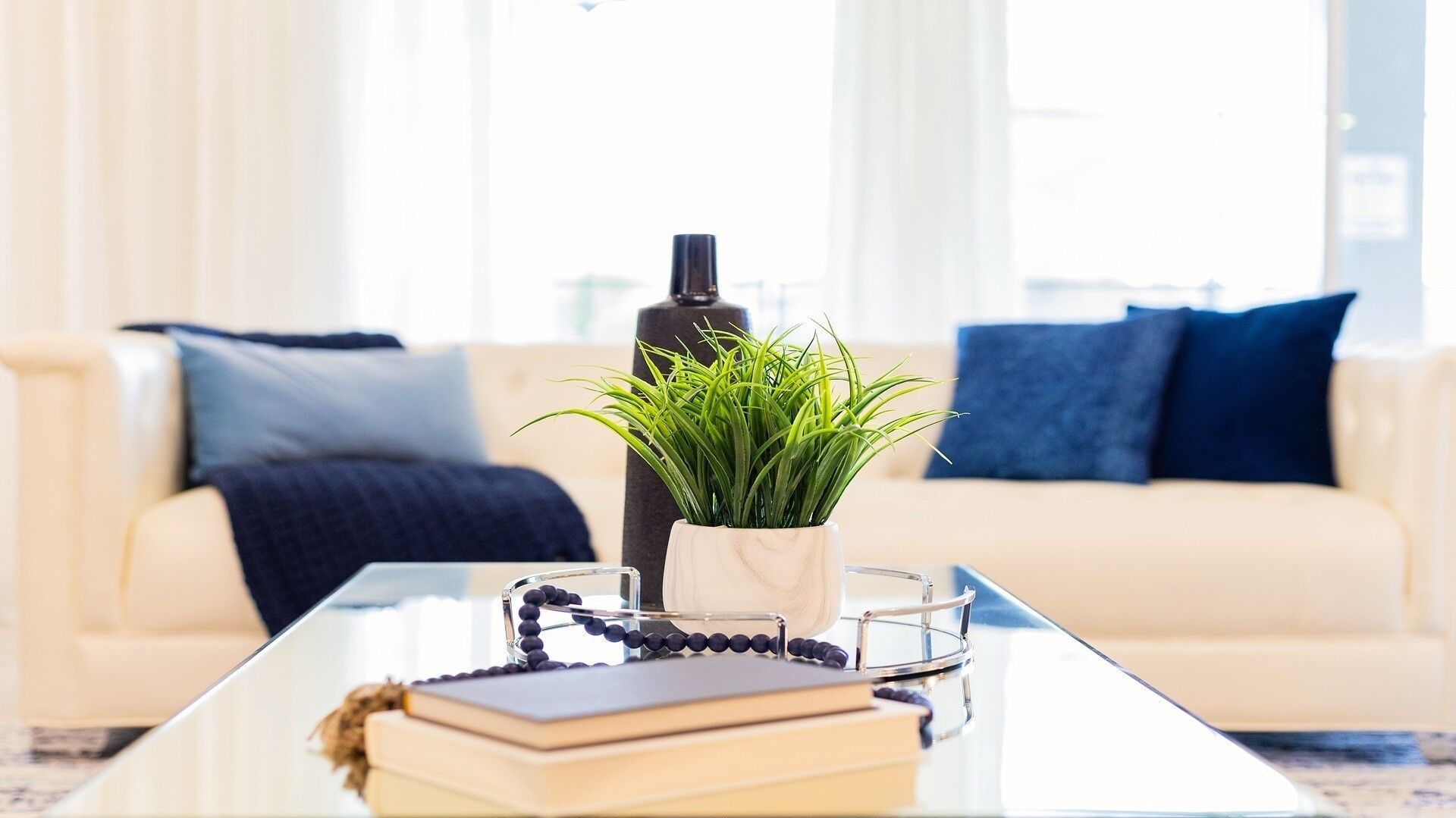 A living room with a glass coffee table, a potted plant, a book, a rosary, and a bottle.