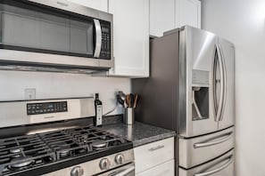 Une cuisine équipée d’un four à micro-ondes, d’un réfrigérateur et d’une cuisinière à gaz, tous en acier inoxydable.