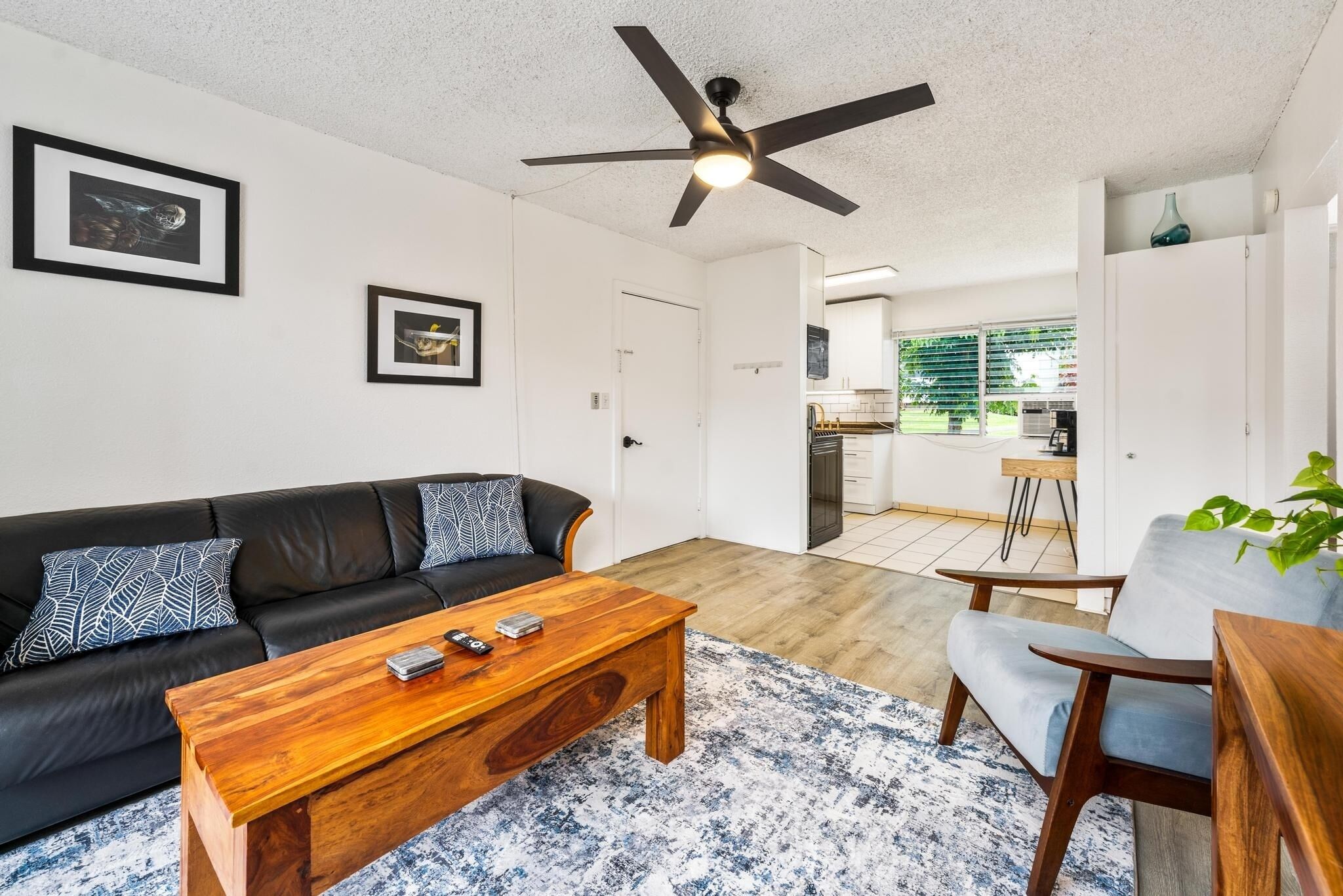 A modern living room with a black leather sofa, a wooden coffee table, and a ceiling fan.