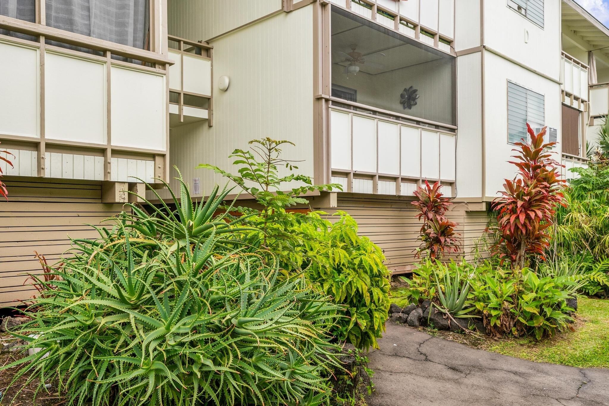 Un edificio residencial con fachada color beige, múltiples ventanas y un pequeño jardín con diversas plantas.