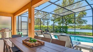 Ein Essbereich am Pool mit Blick auf einen See, Sitzgelegenheiten im Freien und einem Grill.