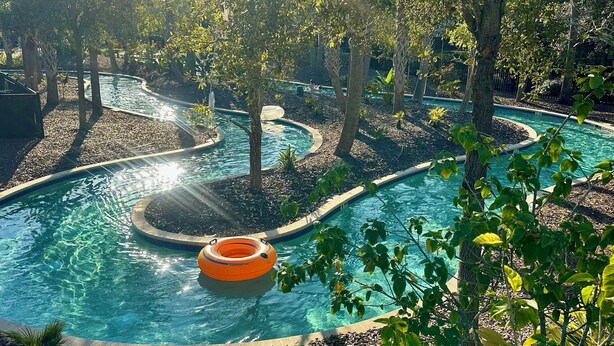 Ein Pool mit geschwungener Form, umgeben von Bäumen und einer kleinen Insel mit einem Brunnen.