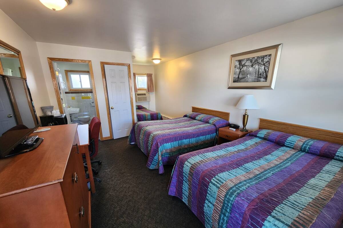 A hotel room with two beds, a desk with a telephone, a mirror, a window with curtains, and a framed picture on the wall.
