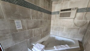 A bathroom with a bathtub, a towel rack, and a wall-mounted air conditioning unit. - Riviera Motel Erie (Erie)