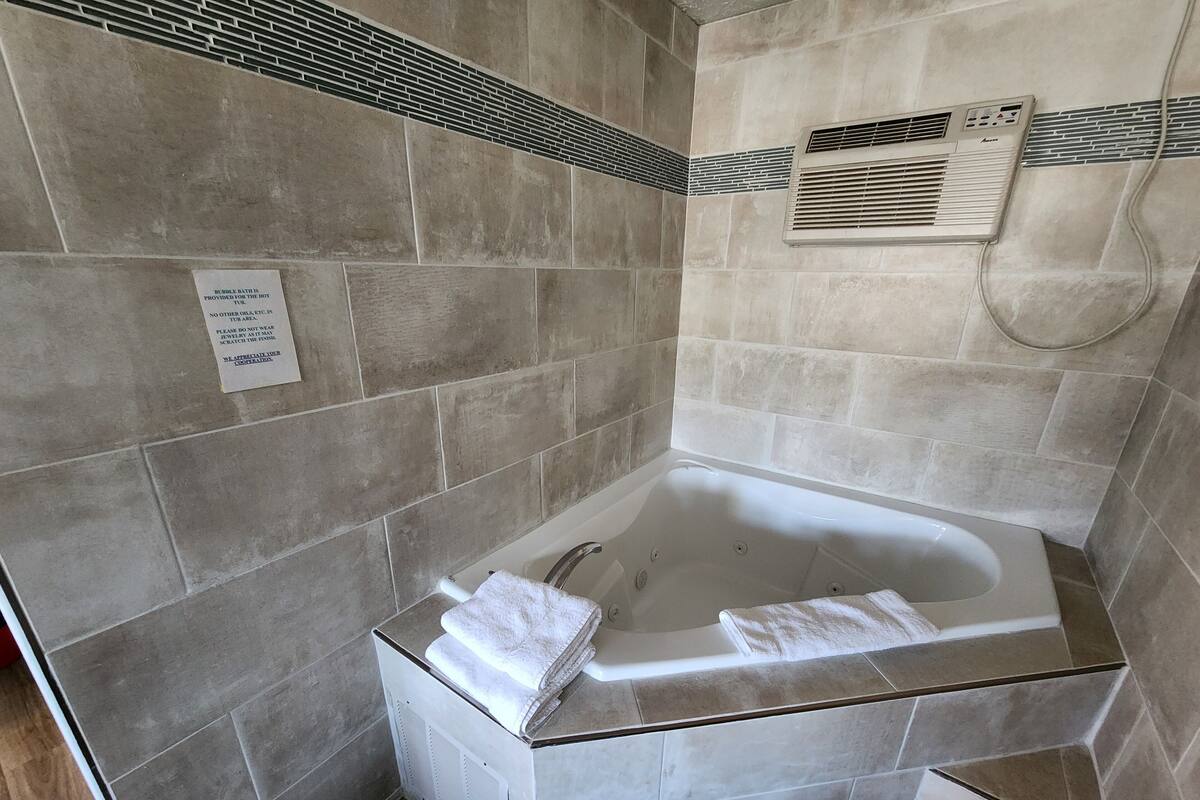 A bathroom with a bathtub, a towel rack, and a wall-mounted air conditioning unit.