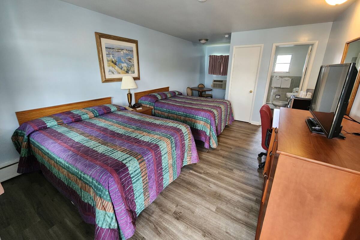 A hotel room with two beds, a desk with a computer, a mirror, and a painting on the wall.