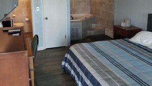 A bedroom with a bed, a desk, a chair, a bathroom with a shower, and a door. - Riviera Motel Erie (Erie)