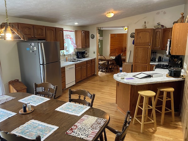 A kitchen with wooden cabinets, a refrigerator, a dining table with chairs, and a bar area with stools. - Hickey Creek Retreat Secluded Log Home - 7 miles from Pictured Rocks Lake shore (Shingleton)