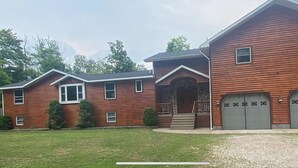 A two-story log cabin with a front porch, a garage, and a well-maintained lawn. - Hickey Creek Retreat Secluded Log Home - 7 miles from Pictured Rocks Lake shore (Shingleton)