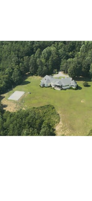 An aerial view of a large, single-story house with a spacious lawn and a tennis court.
