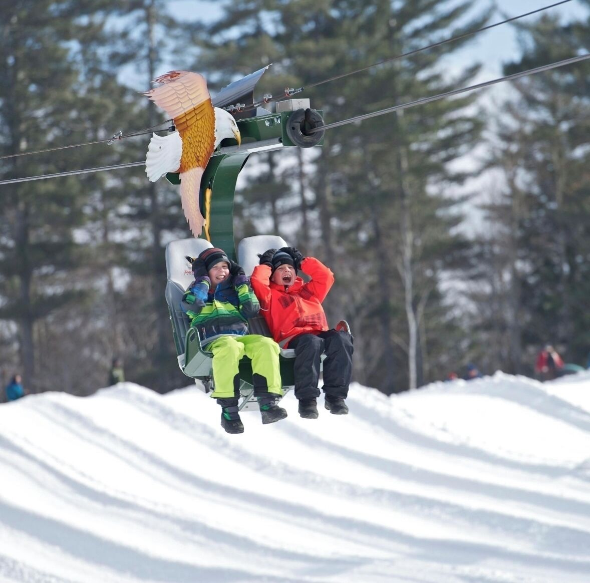 A chairlift carrying passengers over a snowy landscape with trees in the background.