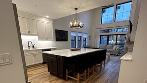 A modern kitchen with a central island, white cabinetry, and a chandelier. - Brand New 2-Story Loft Residence Above Cranmore Mountain Lodge (Conway)