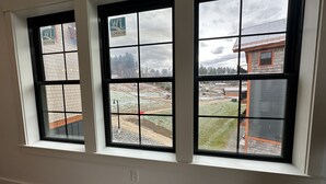 A room with three large windows, each divided into nine panes, offering views of a construction site and surrounding buildings. - Brand New 2-Story Loft Residence Above Cranmore Mountain Lodge (Conway)