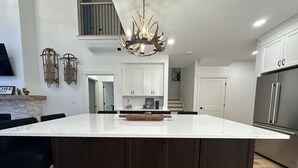 A modern kitchen with a large island, dark cabinetry, and a unique antler chandelier. - Brand New 2-Story Loft Residence Above Cranmore Mountain Lodge (Conway)