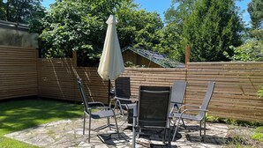 Une terrasse avec un sol en pierre, une table, quatre chaises et un grand parasol.