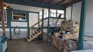 Un espacio al aire libre techado con chimenea de piedra, escaleras de madera y piso de concreto.