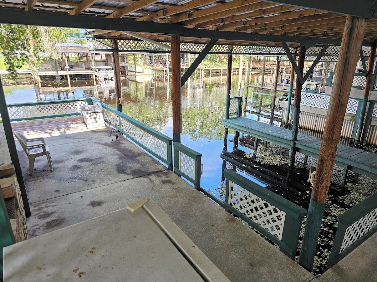 Un espacio al aire libre techado, con piso de concreto, bancos de madera y vistas a un cuerpo de agua.
