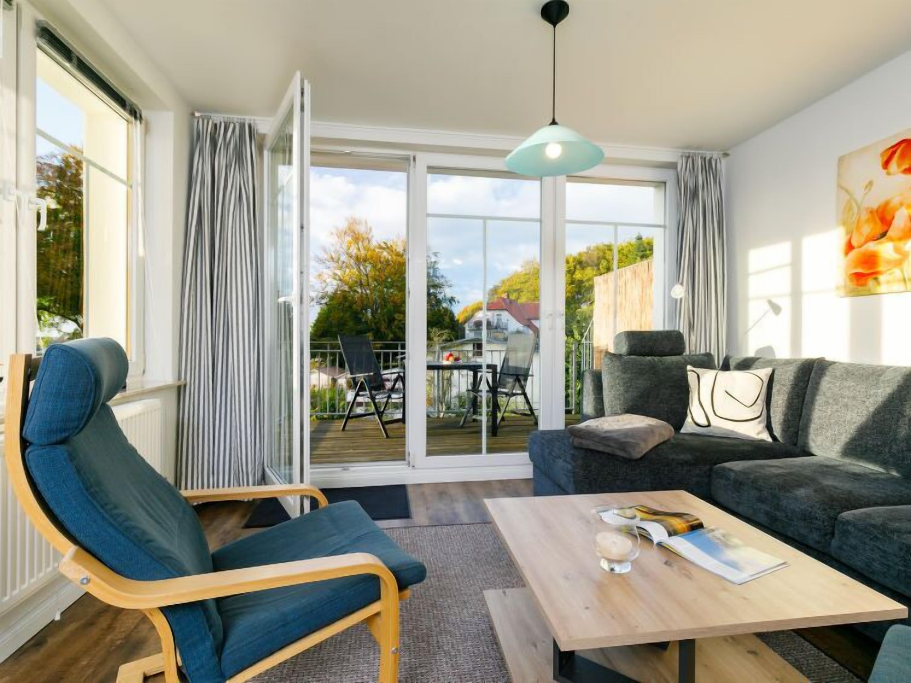 Ein modernes Wohnzimmer mit einer Couch, einem Sessel, einem Tisch und Blick ins Freie durch eine Schiebetür.
