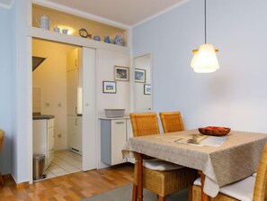 Un coin repas avec une table dressée pour deux personnes, un luminaire suspendu et une vue sur la cuisine.