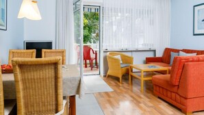 Un salon moderne avec un canapé, une table à manger, des chaises en osier et un téléviseur.