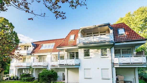 Une maison à deux étages, avec un toit recouvert de tuiles rouges, des murs extérieurs blancs et un balcon à chaque étage.