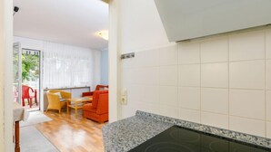 Une cuisine moderne dotée d’une cuisinière intégrée, un coin repas avec des chaises rouges et une vue sur un balcon où se trouve une chaise rouge.