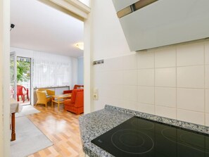 Une cuisine moderne dotée d’une cuisinière intégrée, un coin repas avec des chaises rouges et une vue sur un balcon où se trouve une chaise rouge.