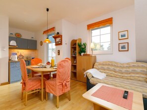 A cozy living room with a sofa, a dining table with chairs, a kitchen area, and a window with curtains. - Apartment Martin by Interhome (Zinnowitz)